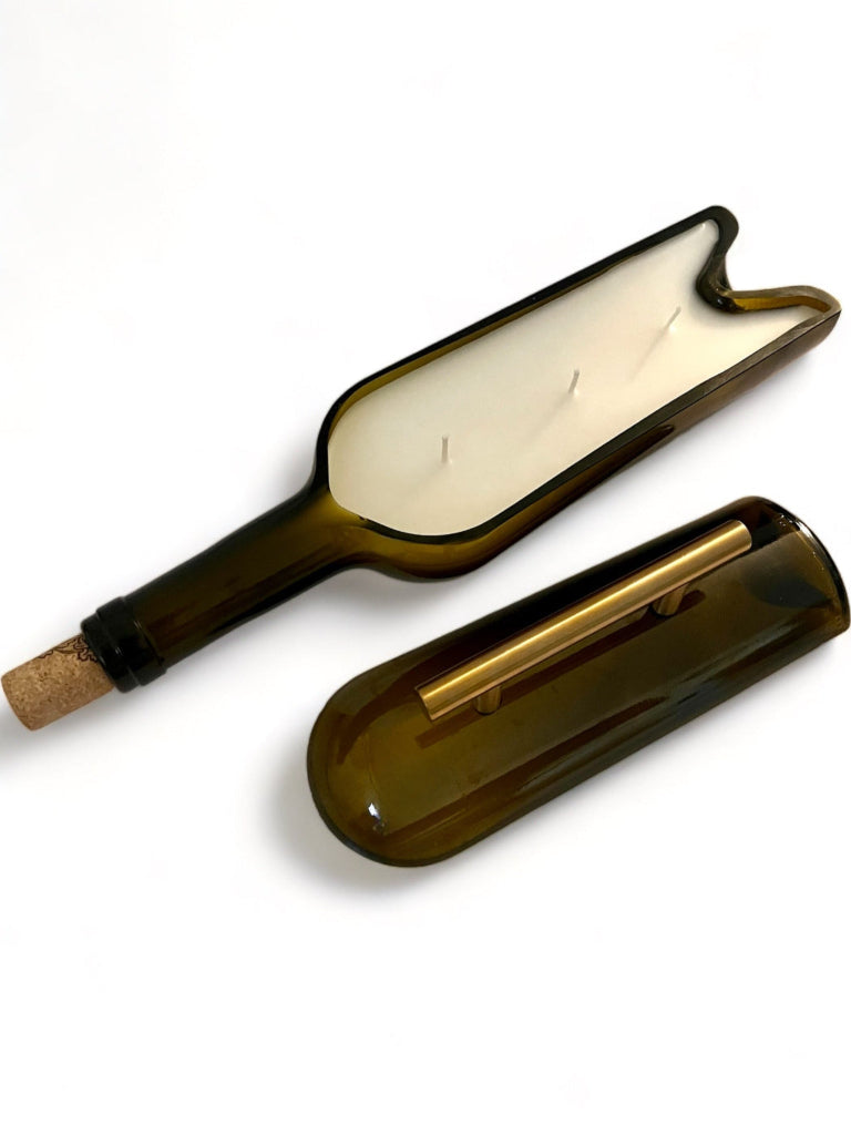 An upcycled wine bottle candle with a cut-out shape for the wick, showing the candle inside the brown bottle with a white wax and a cork stopper.