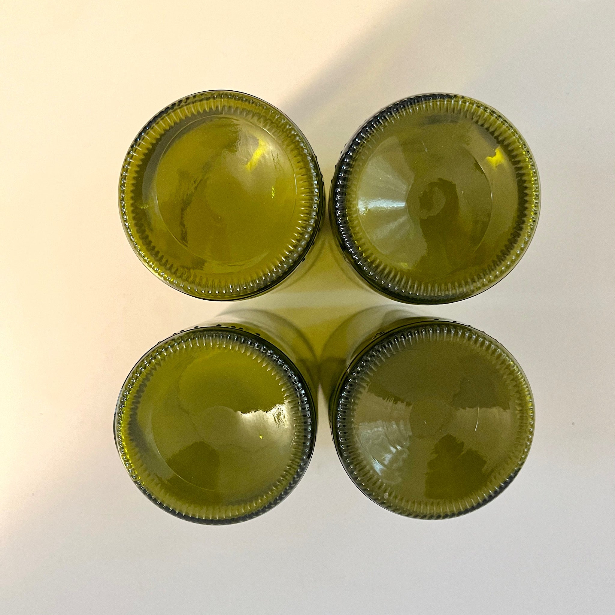 Four 12 oz handcrafted drinking glasses made from recycled wine bottles, displayed on a clean white background, highlighting eco-friendly design and sustainability. Bottom of glasses.