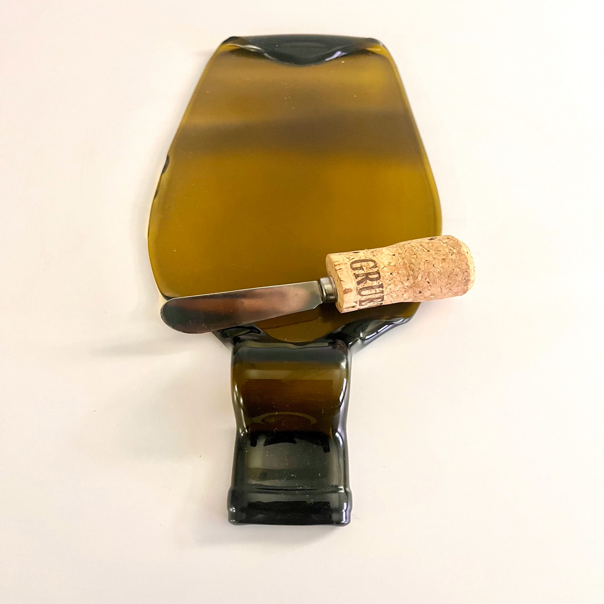 Close-up of an amber repurposed wine bottle cheese board with a smooth, kiln-fired finish and rustic cork spreader knife.